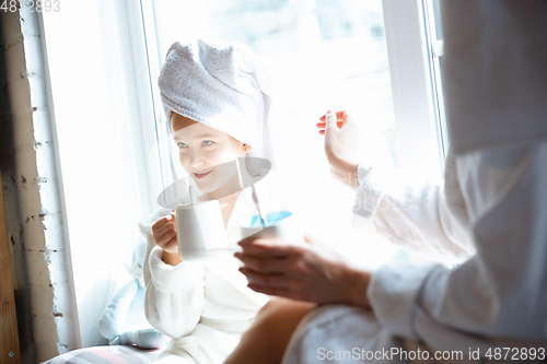 Image of Mother and daughter, sisters have quite, beauty and fun day together at home. Comfort and togetherness. Drinking tea near window wearing white bathrobes