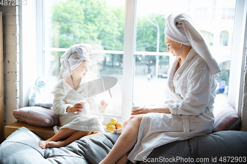 Image of Mother and daughter, sisters have quite, beauty and fun day together at home. Comfort and togetherness. Drinking tea near window wearing white bathrobes