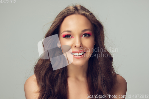 Image of Close up of beautiful young woman with long healthy curly hair and bright make up isolated on grey studio backgroud, smiling with white teeth