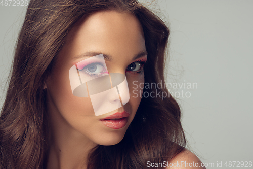 Image of Close up of beautiful young woman with long healthy curly hair and bright make up isolated on grey studio backgroud, looking serious