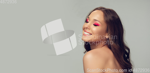 Image of Close up of beautiful young woman with long healthy curly hair and bright make up isolated on grey studio backgroud, flyer with copyspace