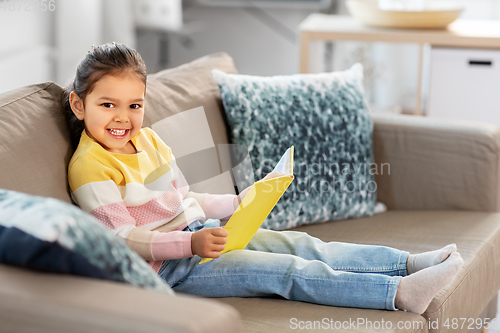 Image of happy smiling little girl reading book at home