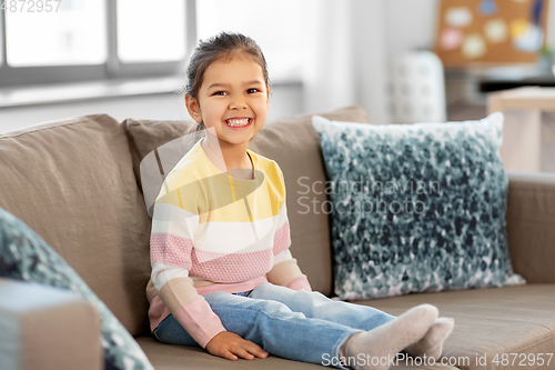 Image of happy smiling little girl sitting on sofa at home