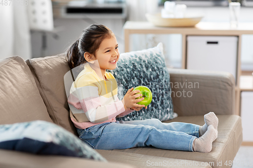Image of happy little girl with apple sitting on sofa