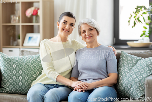 Image of senior mother with adult daughter hugging at home