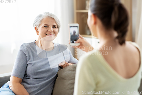 Image of adult daughter photographing senior mother at home