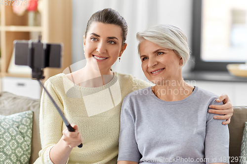 Image of senior mother with daughter taking selfie at home