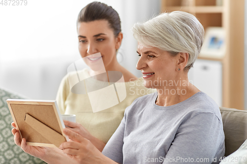 Image of adult daughter and old mother with photo at home