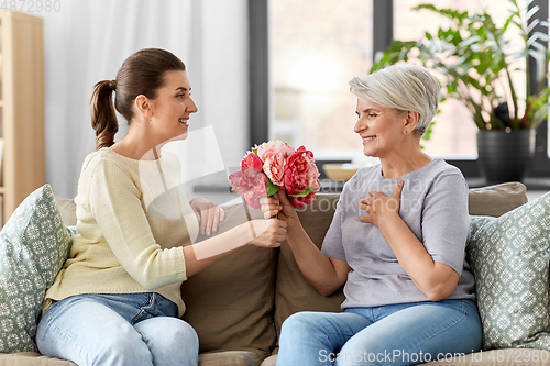 Image of adult daughter giving flowers to old mother