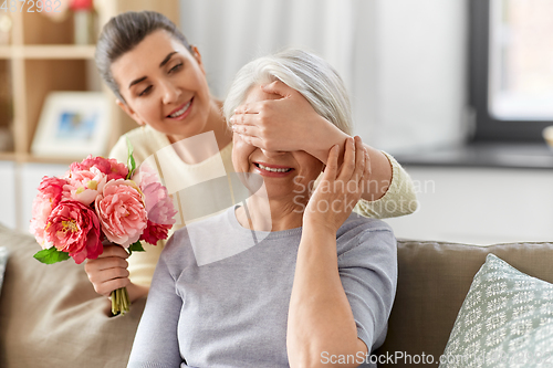 Image of adult daughter giving flowers to old mother