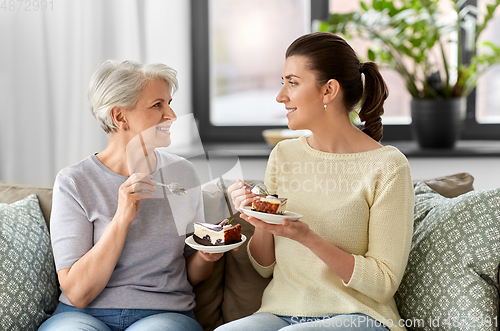 Image of old mother and adult daughter eating cake at home