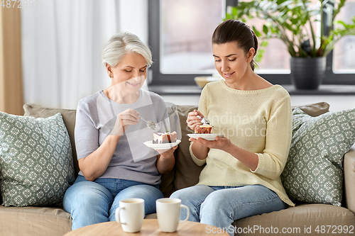 Image of old mother and adult daughter eating cake at home