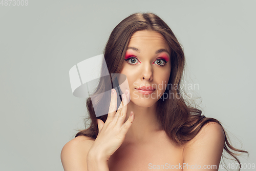 Image of Close up of beautiful young woman with long healthy curly hair and bright make up isolated on grey studio backgroud, soft touching the cheek