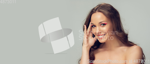 Image of Close up of beautiful young woman with long healthy curly hair and bright make up isolated on grey studio backgroud, flyer with copyspace