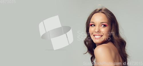 Image of Close up of beautiful young woman with long healthy curly hair and bright make up isolated on grey studio backgroud, flyer with copyspace