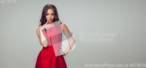 Image of Beautiful young woman with long healthy curly hair and bright make up wearing red dress isolated on grey studio backgroud. Flyer with copyspace.