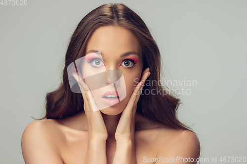 Image of Close up of beautiful young woman with long healthy curly hair and bright make up isolated on grey studio backgroud, shocked with hands on her face