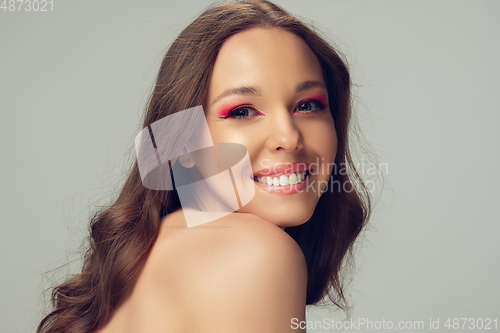 Image of Close up of beautiful young woman with long healthy curly hair and bright make up isolated on grey studio backgroud, shy smiling