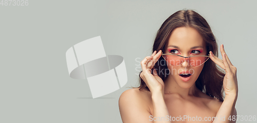 Image of Close up of beautiful young woman with long healthy curly hair and bright make up wearing stylish pink eyewear isolated on grey studio backgroud, flyer with copyspace