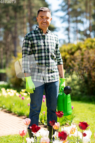 Image of happy man with watering can and flowers at garden