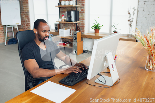 Image of Young man, businessman working in office, looking on computer screen, monitor, with blank white sheet, whiteboard near him. Copyspace.