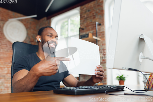 Image of Young man, businessman working in office, looking on blank black computer screen, monitor, holding blank white sheet, whiteboard. Copyspace.