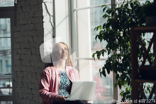Image of Young woman, businesswoman working or studying at home with laptop near window. Attented, concentrated. Copyspace.
