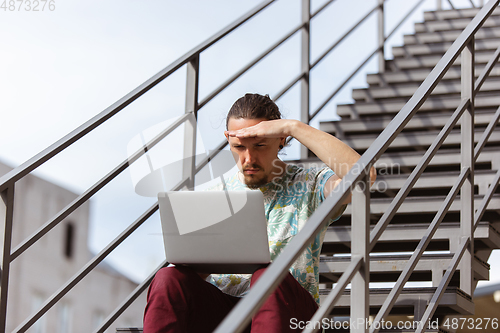 Image of Young man, businessman working, studying outdoors, looking on computer screen, monitor. Copyspace.