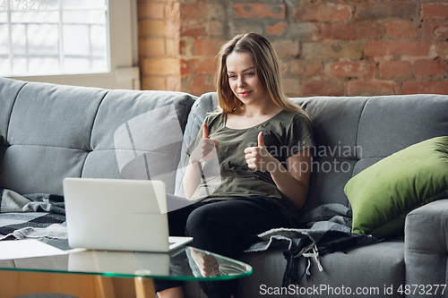 Image of Young woman, businesswoman working or studying at home with laptop sitting on sofa. Attented, concentrated. Copyspace.