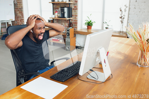 Image of Young man, businessman working in office, looking on computer screen, monitor, with blank white sheet, whiteboard near him. Copyspace.