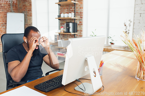 Image of Young man, businessman working in office, looking on computer screen, monitor, with blank white sheet, whiteboard near him. Copyspace.