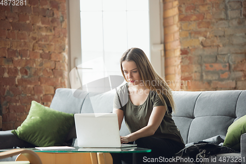 Image of Young woman, businesswoman working or studying at home with laptop sitting on sofa. Attented, concentrated. Copyspace.