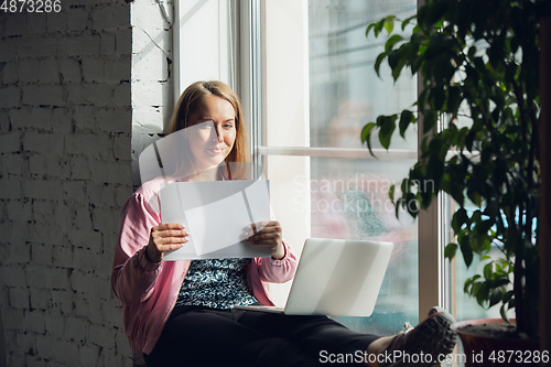 Image of Young woman, businesswoman working or studying at home holding white sheet, whiteboard. Attented, concentrated. Copyspace. Top view.