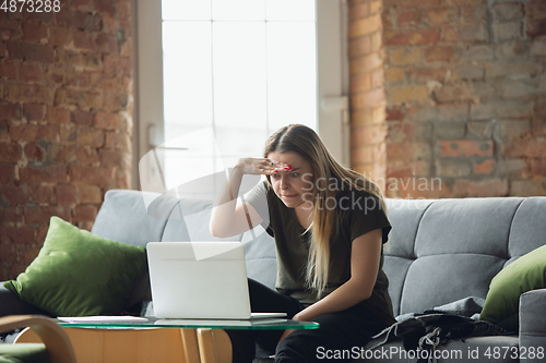 Image of Young woman, businesswoman working or studying at home with laptop sitting on sofa. Attented, concentrated. Copyspace.