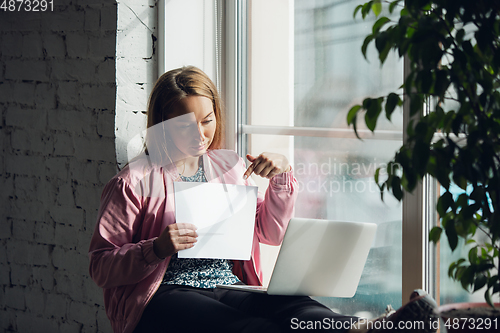 Image of Young woman, businesswoman working or studying at home holding white sheet, whiteboard. Attented, concentrated. Copyspace. Top view.