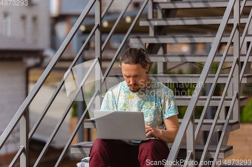 Image of Young man, businessman working, studying outdoors, looking on computer screen, monitor. Copyspace.