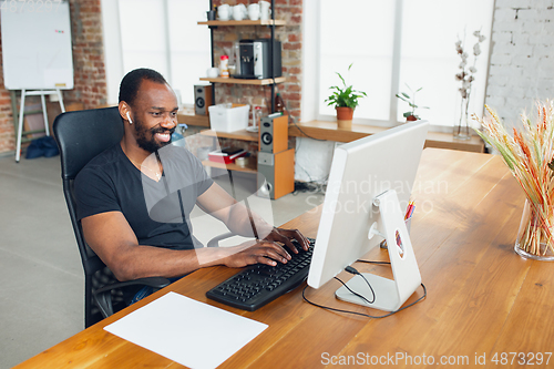 Image of Young man, businessman working in office, looking on computer screen, monitor, with blank white sheet, whiteboard near him. Copyspace.
