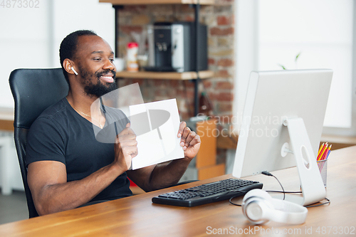 Image of Young man, businessman working in office, looking on blank black computer screen, monitor, holding blank white sheet, whiteboard. Copyspace.