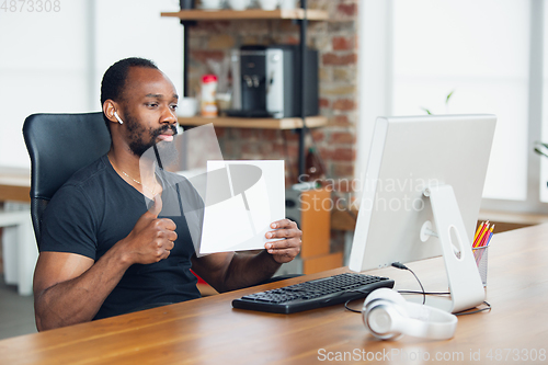 Image of Young man, businessman working in office, looking on blank black computer screen, monitor, holding blank white sheet, whiteboard. Copyspace.