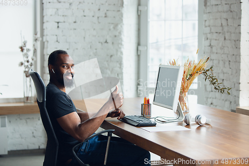 Image of Young man, businessman working in office, looking on blank black computer screen, monitor. Copyspace.