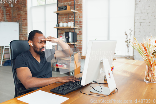 Image of Young man, businessman working in office, looking on computer screen, monitor, with blank white sheet, whiteboard near him. Copyspace.