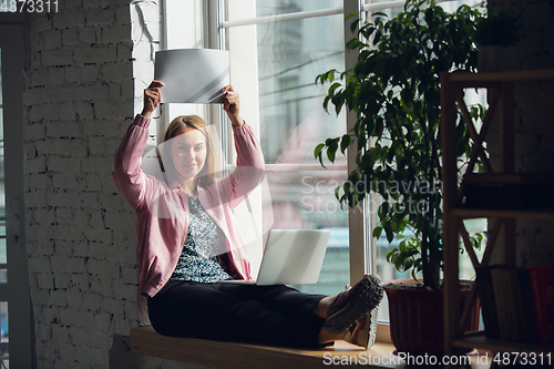 Image of Young woman, businesswoman working or studying at home holding white sheet, whiteboard. Attented, concentrated. Copyspace. Top view.