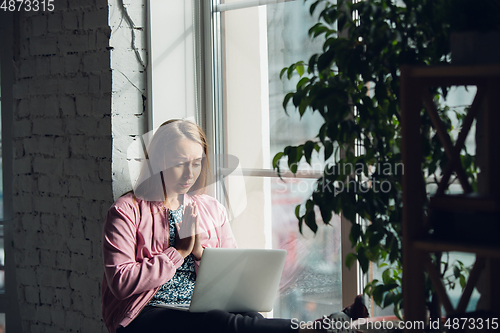 Image of Young woman, businesswoman working or studying at home with laptop near window. Attented, concentrated. Copyspace.