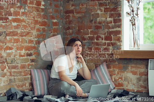 Image of Young woman, businesswoman working or studying at home with laptop near window. Attented, concentrated. Copyspace.