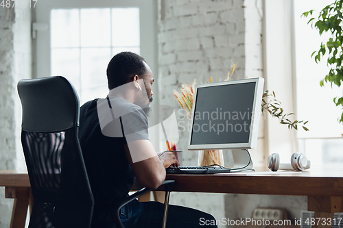 Image of Young man, businessman working in office, looking on blank black computer screen, monitor. Copyspace.