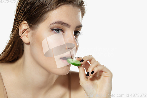 Image of Youth secrets. Close up of beautiful young woman with cucumber slices over white background. Cosmetics and makeup, natural and eco treatment, skin care.