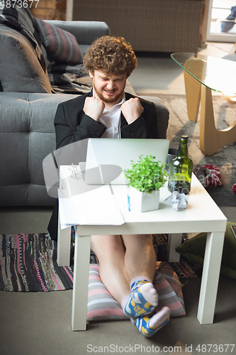 Image of Young man without pants but in jacket working on a computer, laptop. Remote office during coronavirus, fun and comfortable work in underpants