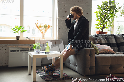 Image of Young man without pants but in jacket working on a computer, laptop. Remote office during coronavirus, fun and comfortable work in underpants