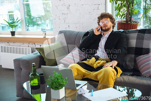 Image of Young man in pajama and jacket working on a computer, laptop. Remote office during coronavirus, fun and comfortable work in underpants