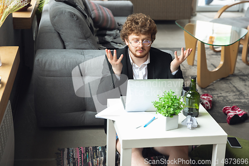 Image of Young man without pants but in jacket working on a computer, laptop. Remote office during coronavirus, fun and comfortable work in underpants